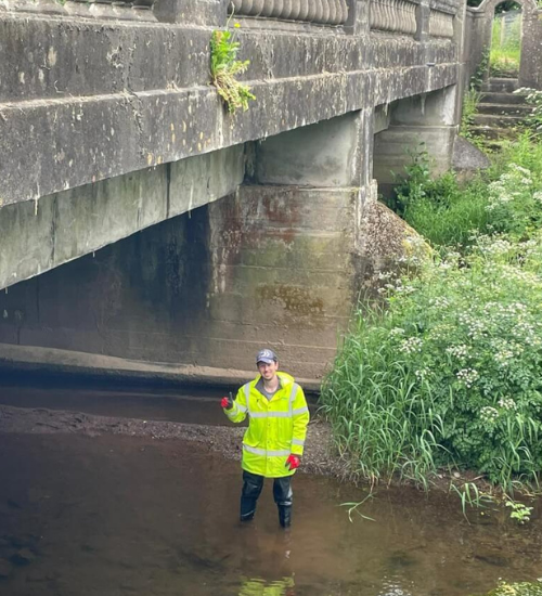 man in high visibility jacket standing under a bridge