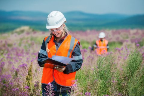 This is an image of a lady wearing safety equipment standing in a field taking notes