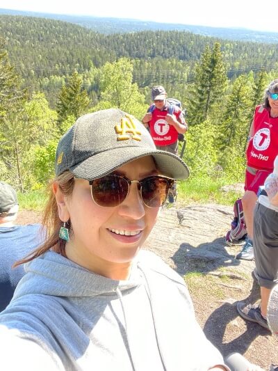 sara smiling at the camera wearing a baseball cap in a beautiful forest 