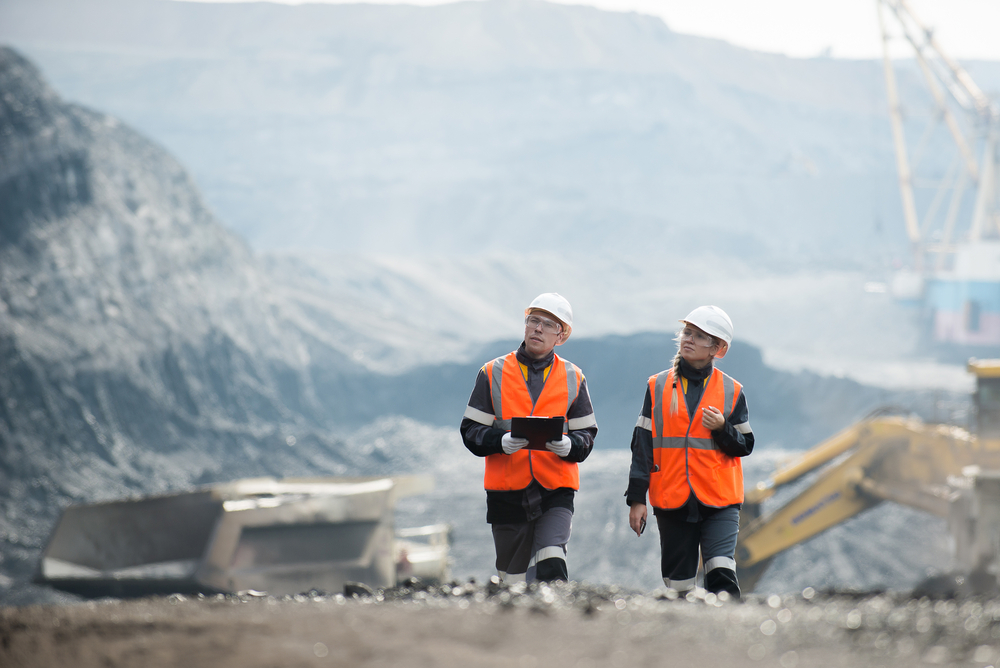 man and woman wearing high visibility jackets and hard hats walking through building site