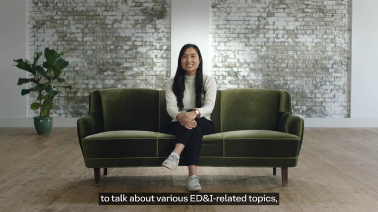A woman sits on a green velvet sofa in a modern room with a whitewashed brick wall and wooden floor. She is smiling, hands folded, and the subtitle reads, "to talk about various ED\&I-related topics."