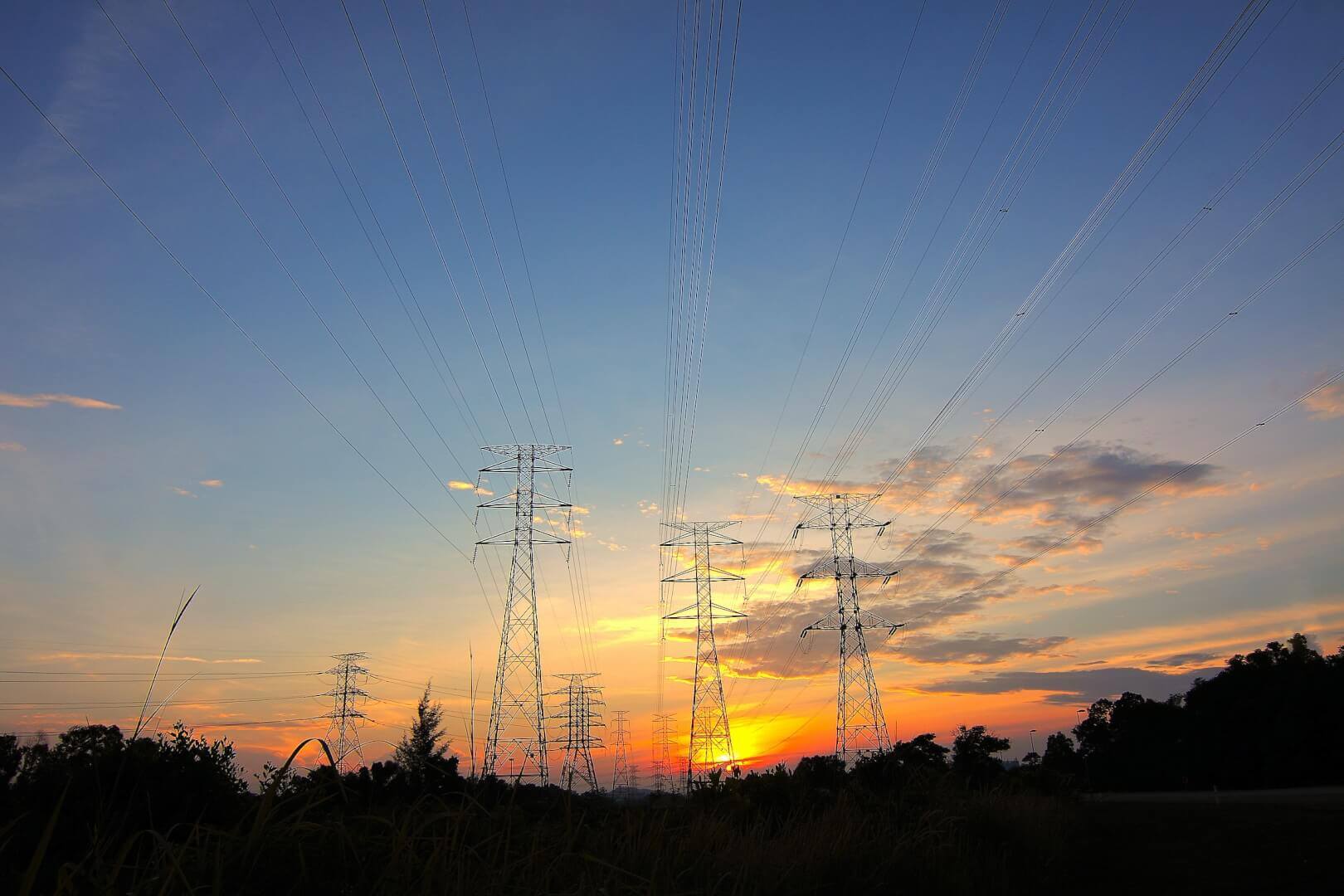 Electrical transmission towers silhouetted against sunset sky