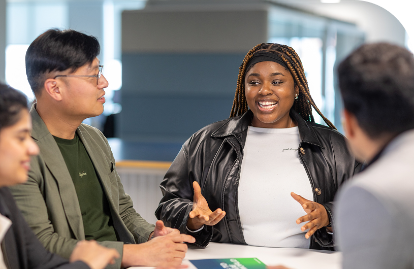 Group of diverse individuals engaged in a lively discussion at a table in a modern office environment.