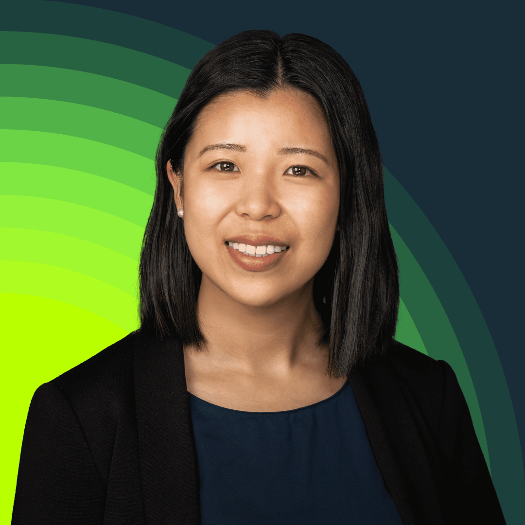 A woman with shoulder-length black hair, wearing a dark blazer and navy top, smiling with a stylized green/blue background.