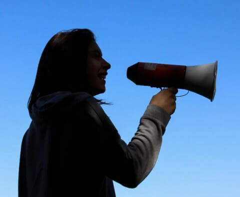 Woman speaking through megaphone under blue sky