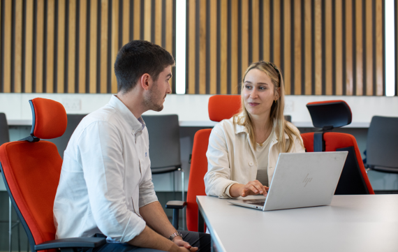 two young professionals collaborating in an office environment with a laptop kept on a table