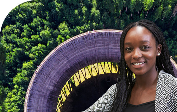 Smiling woman standing in front of a large circular industrial structure surrounded by trees.