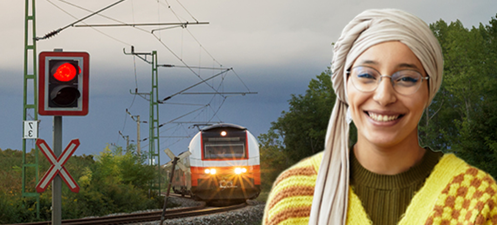 Smiling young man standing in front of an aerial view of a large, green highway interchange with a city skyline in the background.
