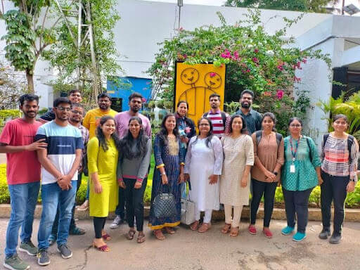 Smiling volunteers and staff standing outdoors in front of a garden and building.