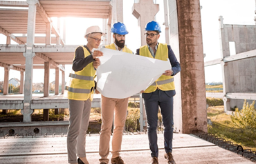 three people on a construction site wearing hard hats, consulting some large plans