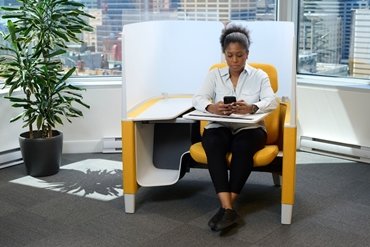 young woman sat in pod at an AtkinsRéalis office typing on a mobile phone 