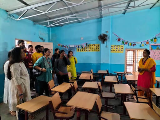 Volunteers and teachers interacting with children inside a bright classroom.
