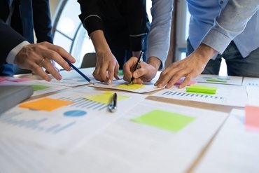 Close up diverse employees working on financial project statistics or report, writing notes on colorful sticky papers, checking documents, coworkers developing business strategy, teamwork