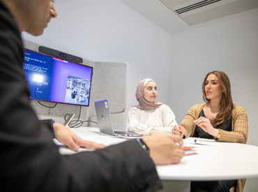three AtkinsRéalis colleagues around a table, smiling and discussing a project