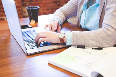 A person working on the laptop and a note book next to the laptop