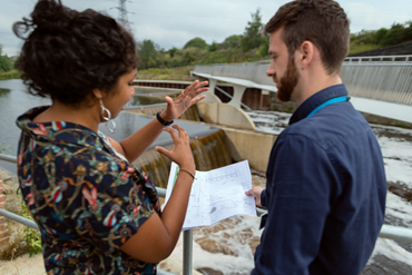 a male and female engineer looking at a water facility and discussing plans 