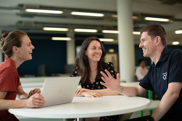 three AtkinsRéalis colleagues around a table, smiling and discussing 