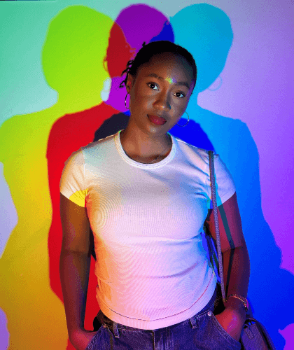 Woman in a white shirt standing against a colorful shadow wall with red, yellow, blue, and purple silhouettes.