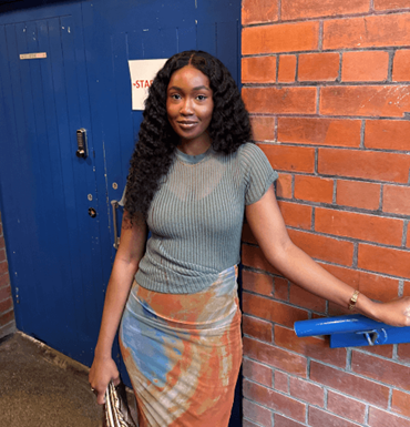 Smiling woman with long curly hair sitting in front of a red brick wall.
